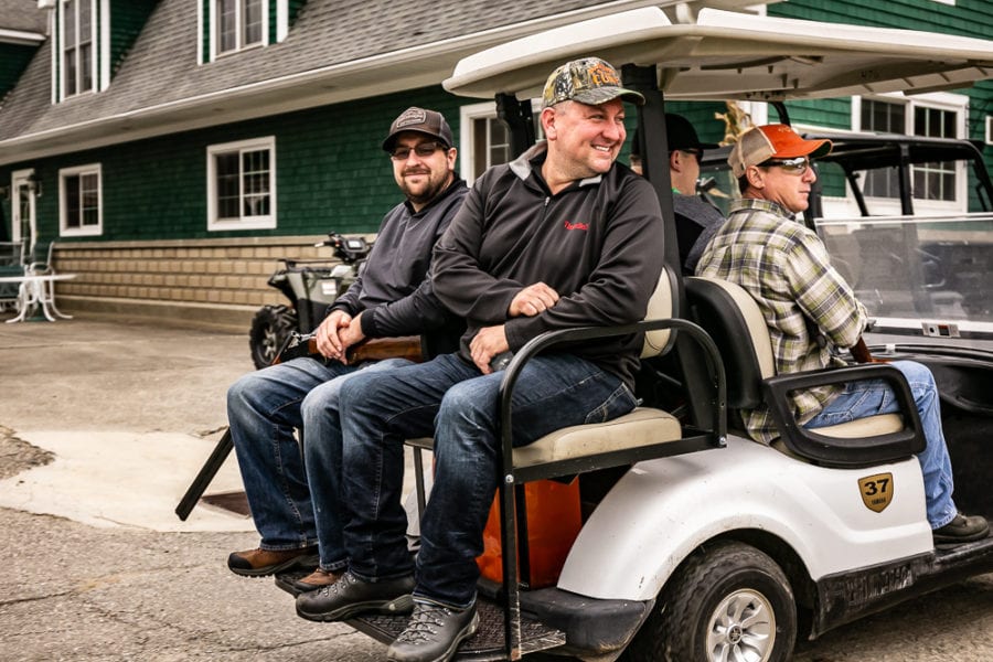 Three men sitting on back of golf cart