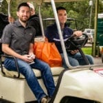Two men in golf cart with orange bag