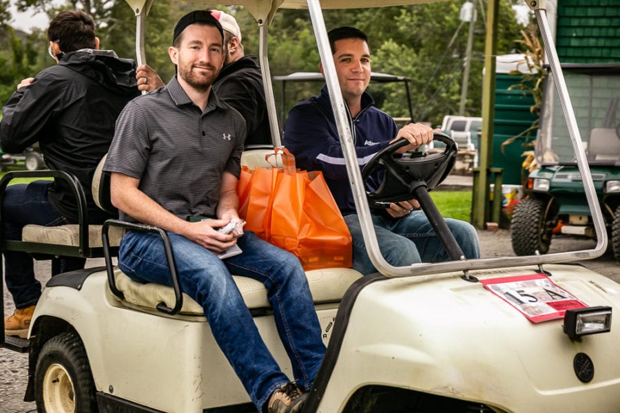 Two men in golf cart with orange bag