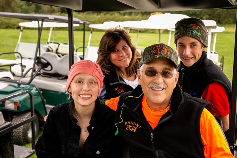 Four smiling people beside golf carts